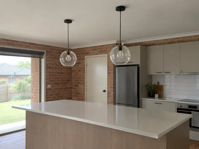 Two glass pendant lights over a kitchen island in a brick-walled home in Woongarrah